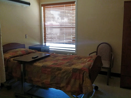 A quiet hospital patient room with a bed, adjacent furniture, and natural light coming through the window.