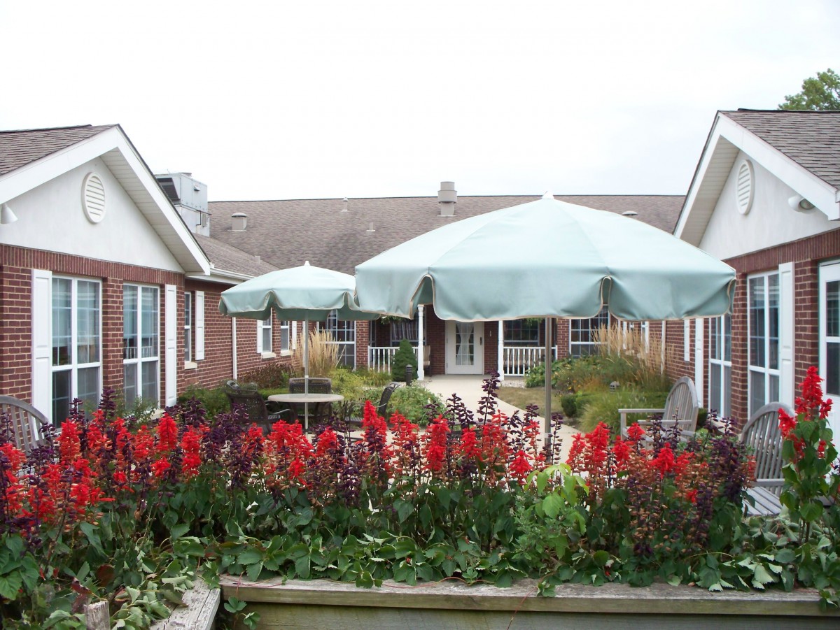 A beautiful garden patio with colorful flowers and large umbrellas in front of a brick building.