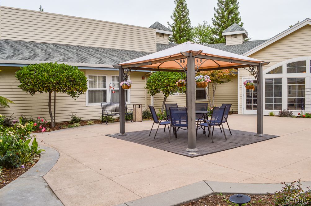 A cozy outdoor patio area featuring a gazebo with chairs and a table, surrounded by landscaped greenery.
