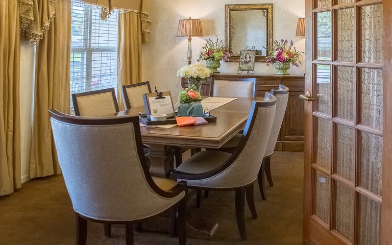 A beautifully decorated dining room with a wooden table and upholstered chairs, featuring elegant lighting and floral arrangements.