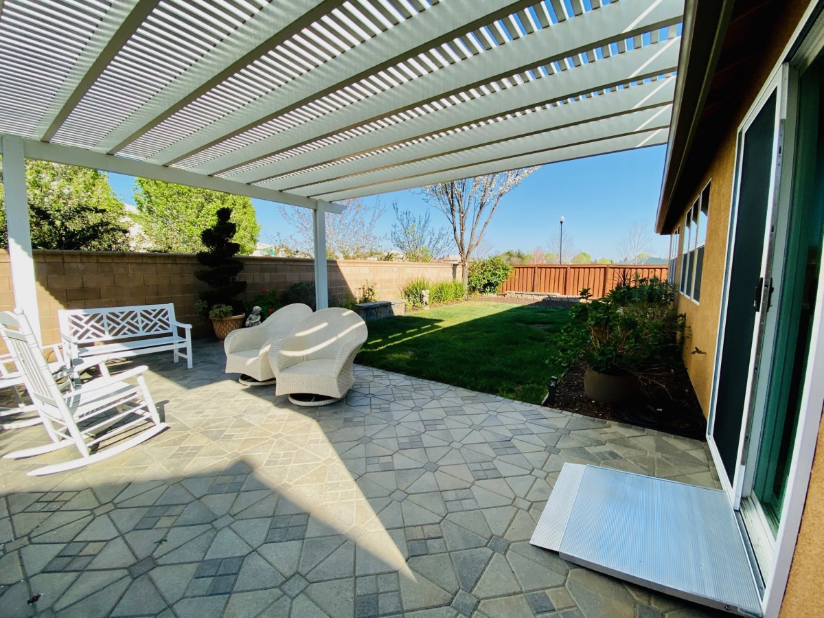 A sunny backyard patio with a pergola and outdoor seating overlooking a well-maintained lawn.