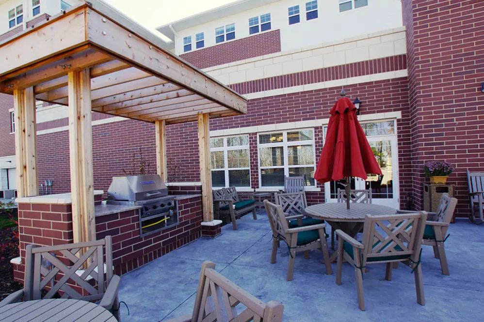 A cozy outdoor patio area with a grill, wooden furniture, and a red umbrella.