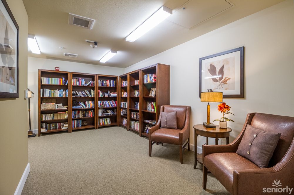 A cozy reading room with bookshelves, chairs, and a lamp.