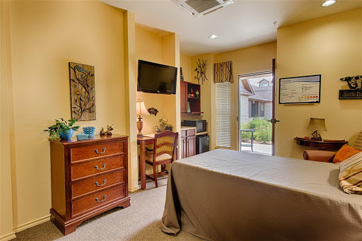 A cozy and well-furnished bedroom featuring a bedside dresser, desk area, and a view through the window.