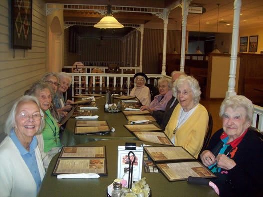 A group of seniors gathered around a table in a restaurant, looking at menus.