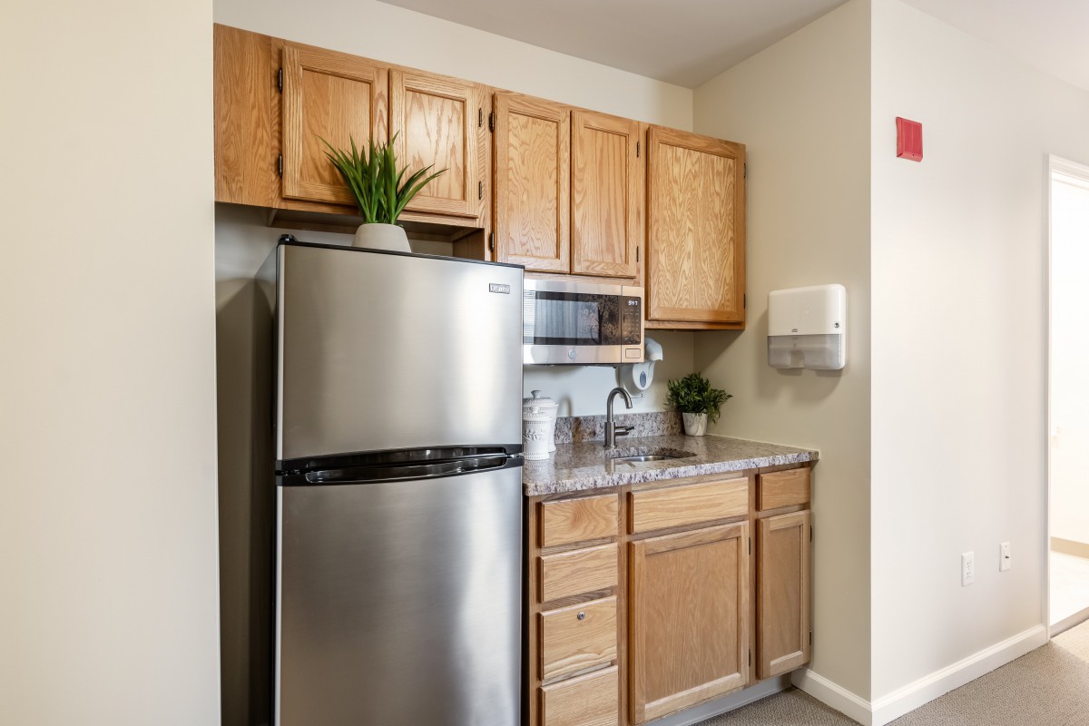 A modern kitchen with wooden cabinets, a stainless steel refrigerator, and a microwave.