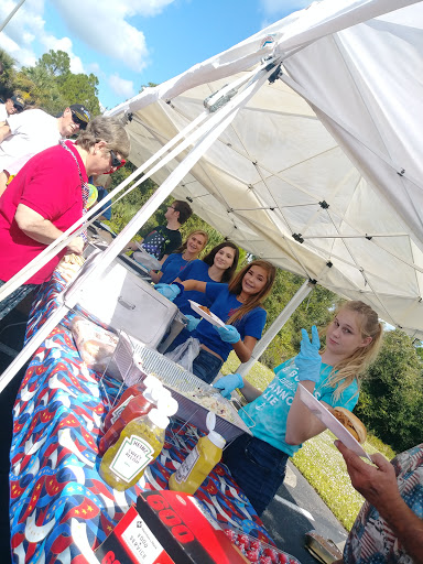 Volunteers serving food at a community event under a tent.