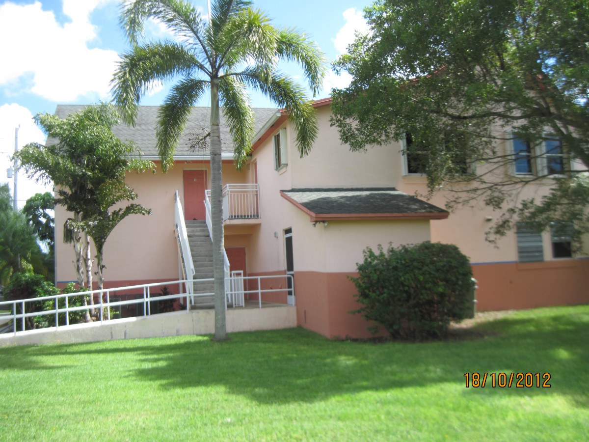An apartment building with palm trees and a well-maintained grassy lawn on a sunny day.