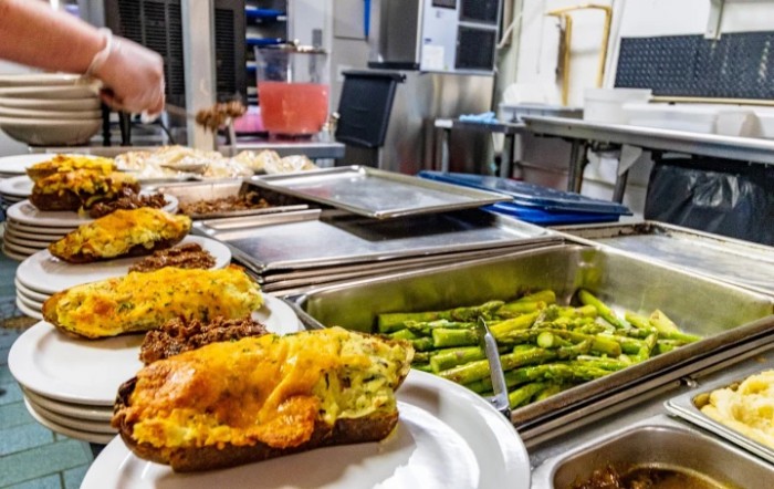 A buffet setup featuring stuffed potatoes with melted cheese and a tray of asparagus in a kitchen setting.