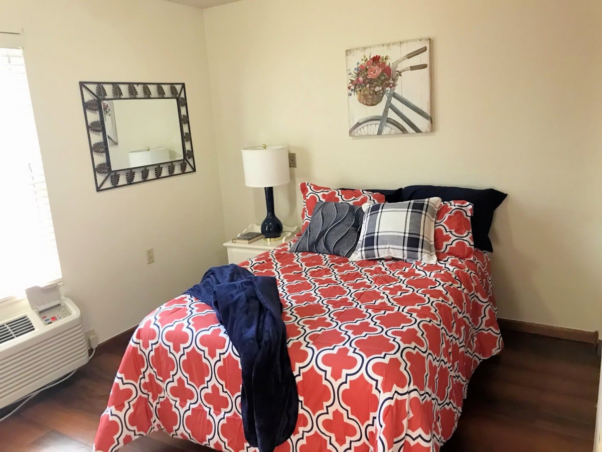 A cozy bedroom with bright red patterned bedding, stylish pillows, and a decorative wall mirror.
