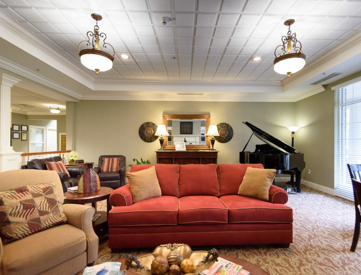 A cozy living room with a red sofa, piano, and elegant chandeliers.
