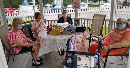 A small gathering of people enjoying food and conversation outdoors while observing safety protocols.