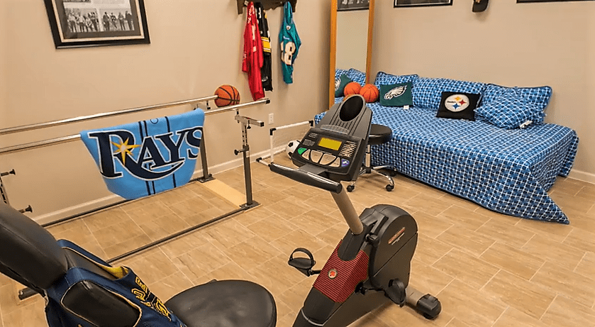 A home gym setup featuring an exercise bike, sports-themed decor, and jerseys on display.