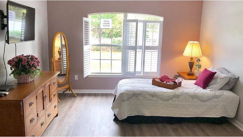A cozy bedroom with a large window, featuring a bed, dresser, and lamp.