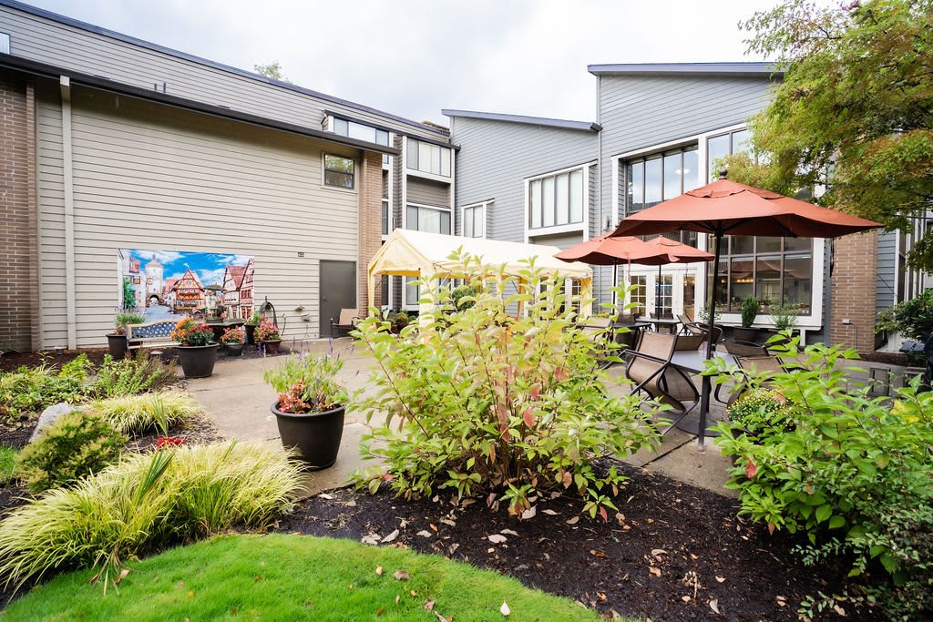 A well-maintained outdoor patio and garden area with seating, umbrellas, and landscaping outside a modern building.