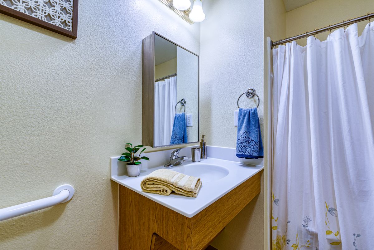 A tidy bathroom with a sink, mirror, and towels arranged neatly.