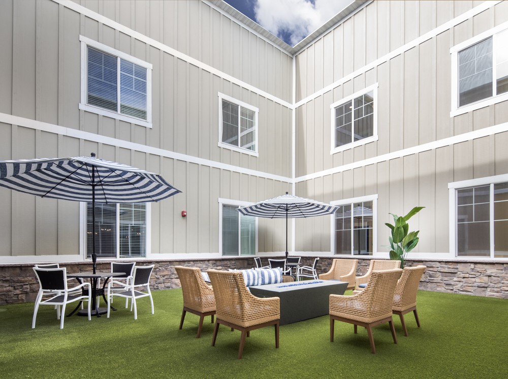 A cozy outdoor patio area with seating and umbrellas, surrounded by a building with multiple windows.