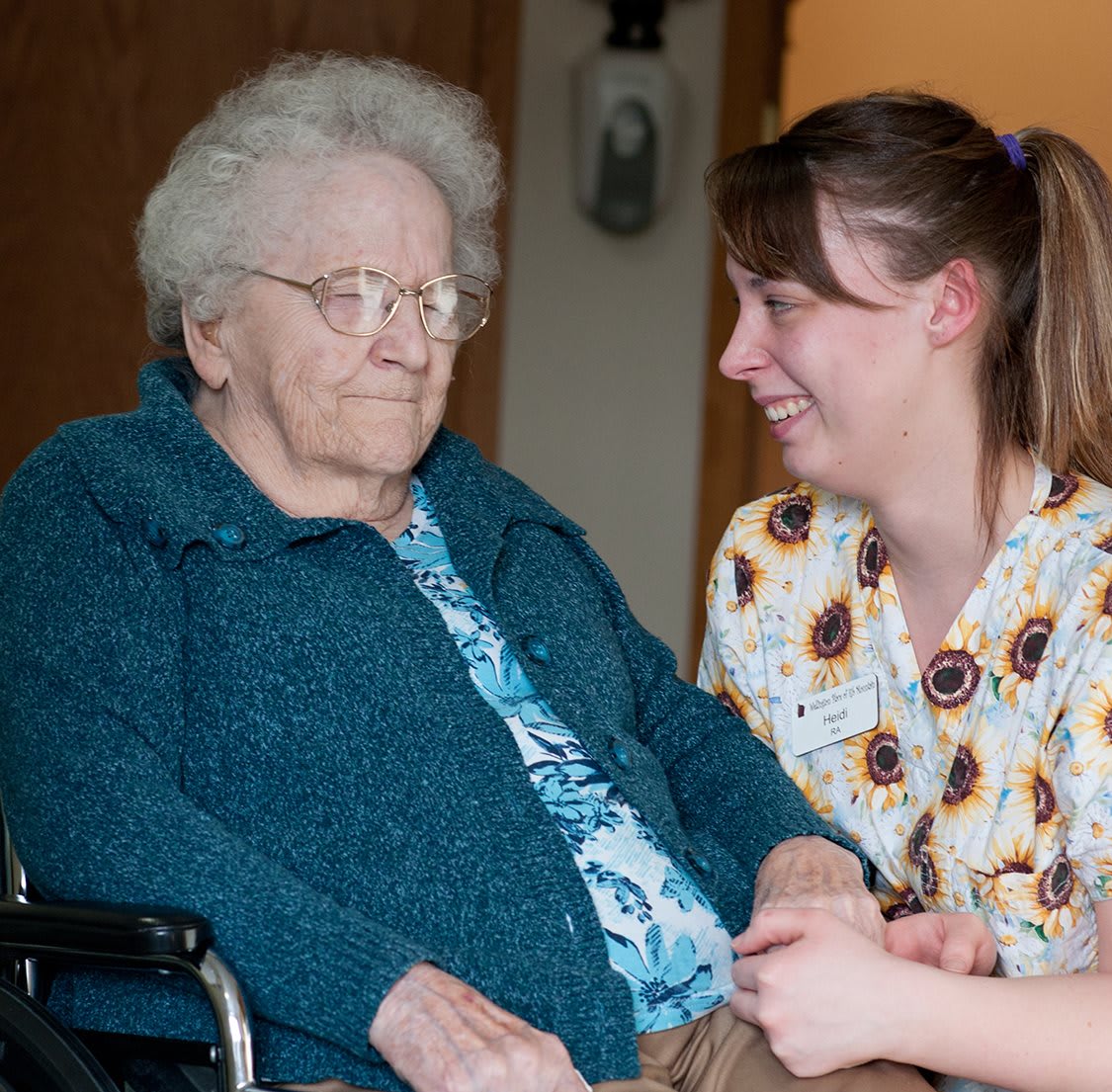 A nurse interacts warmly with an elderly woman in a wheelchair.