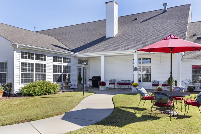 A cozy backyard patio with outdoor furniture and a red umbrella.