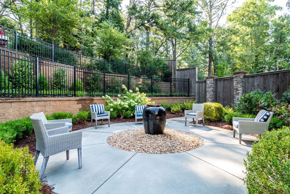 A serene outdoor patio area with chairs surrounding a central fire pit, set against a lush garden backdrop.