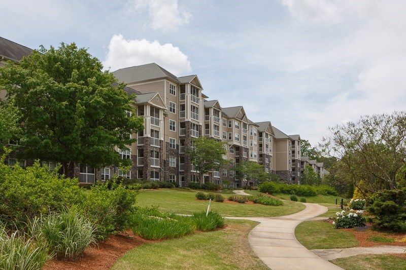 A modern apartment building with landscaped grounds and a winding pathway on a cloudy day.