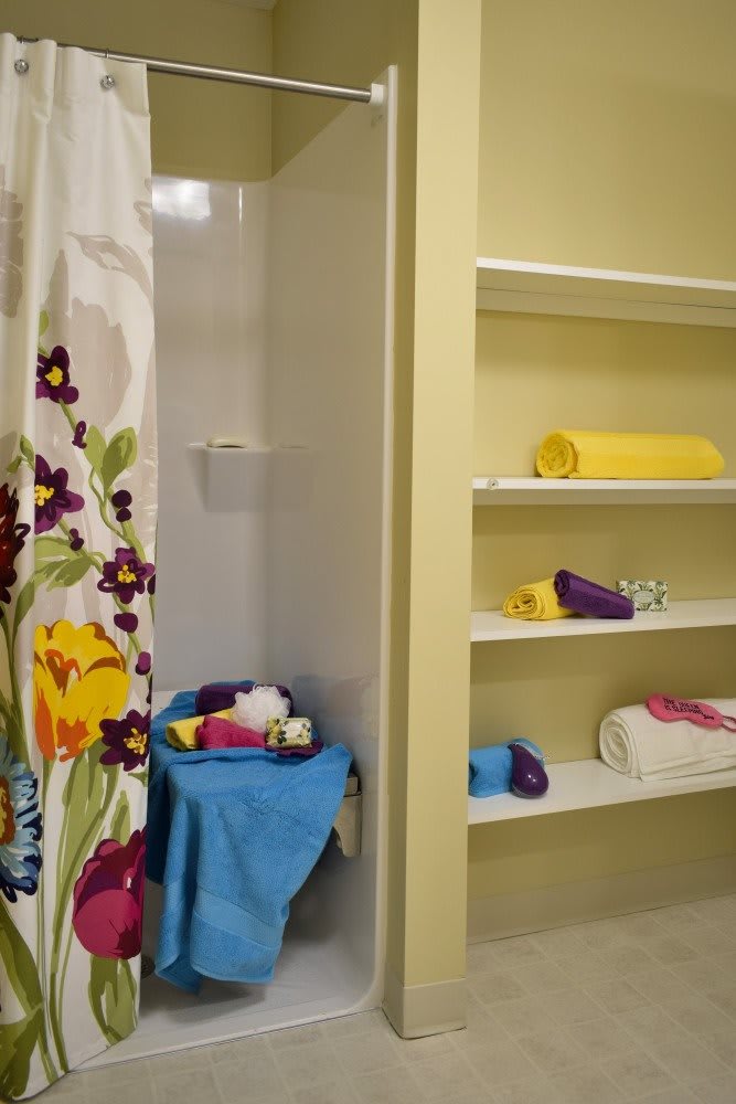 A bathroom with a floral shower curtain and neatly arranged towels on open shelves.