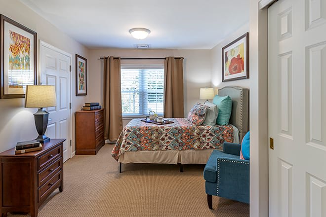 A cozy bedroom with a colorful bedspread, comfortable chair, and natural light streaming through the window.