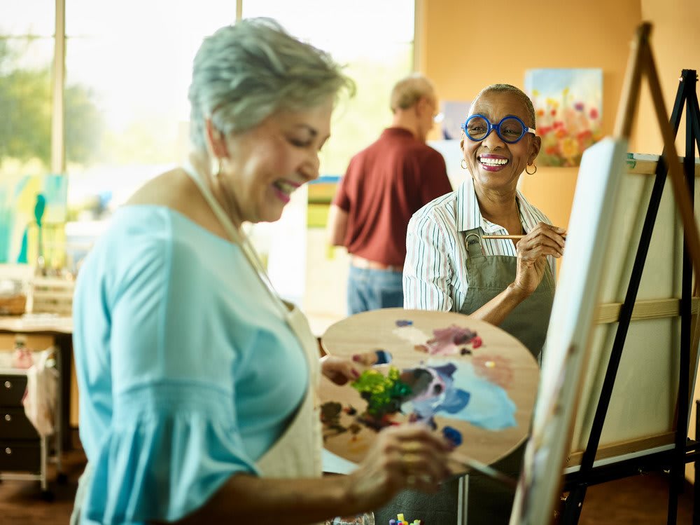 Two people enjoying time together in an art class, painting with palettes and easels.