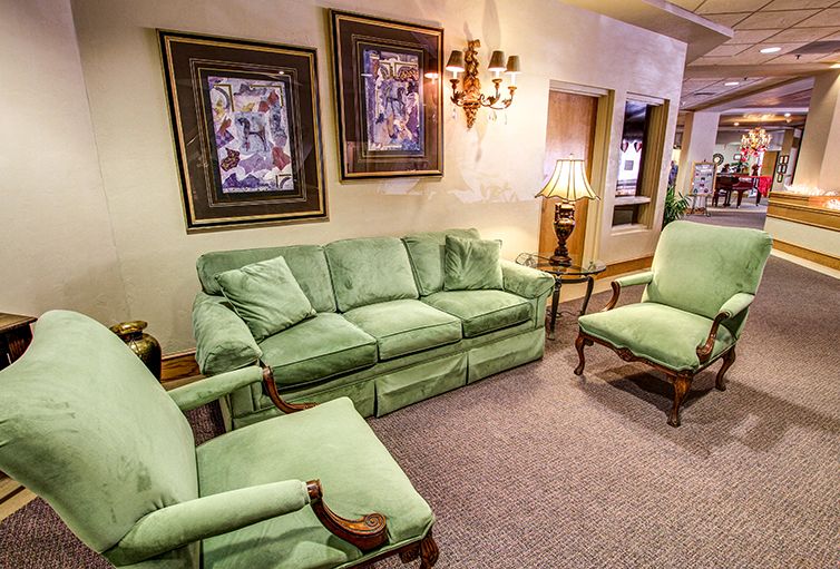 A cozy living room with green upholstered furniture and framed artwork on the walls.