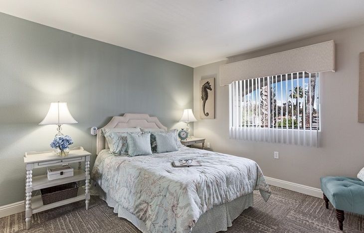 A cozy bedroom with a neatly made bed, soft lighting from bedside lamps, and a window providing natural light.