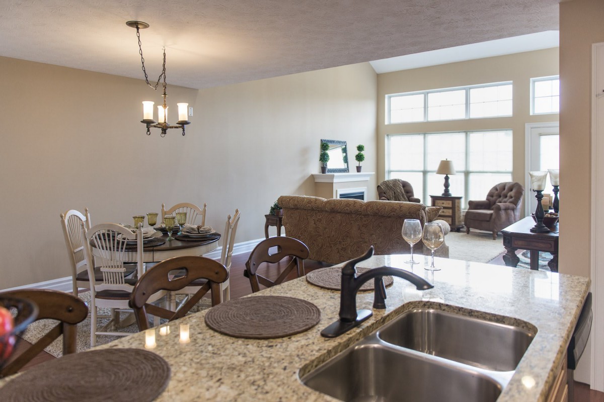 An open-concept living space featuring a kitchen with granite countertops and a sink, adjacent to a dining area, and a cozy living room with large windows.