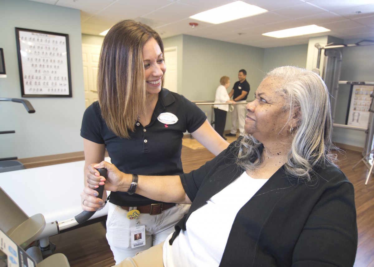 A healthcare professional assisting an elderly woman with physical therapy.