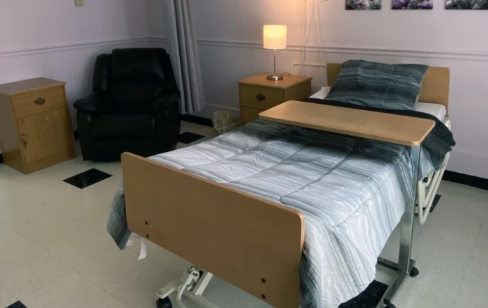 A tidy hospital room with a bed, lamp, and chair.