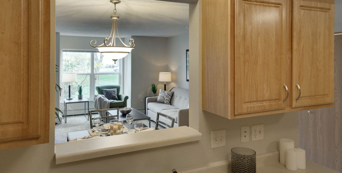 A modern open-concept living and dining area viewed from the kitchen, featuring stylish furniture and a chandelier.
