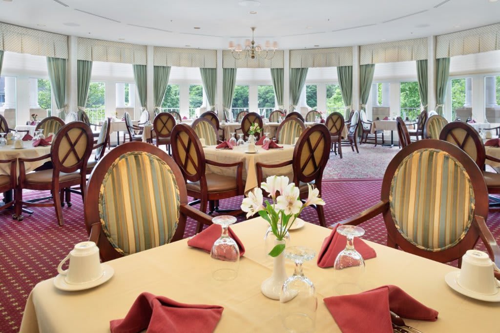 An elegantly decorated dining room with neatly arranged tables and chairs, featuring red napkins and floral centerpieces.