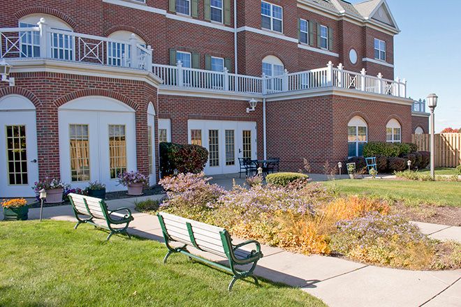 A brick building with balconies and a landscaped garden featuring benches in the foreground.