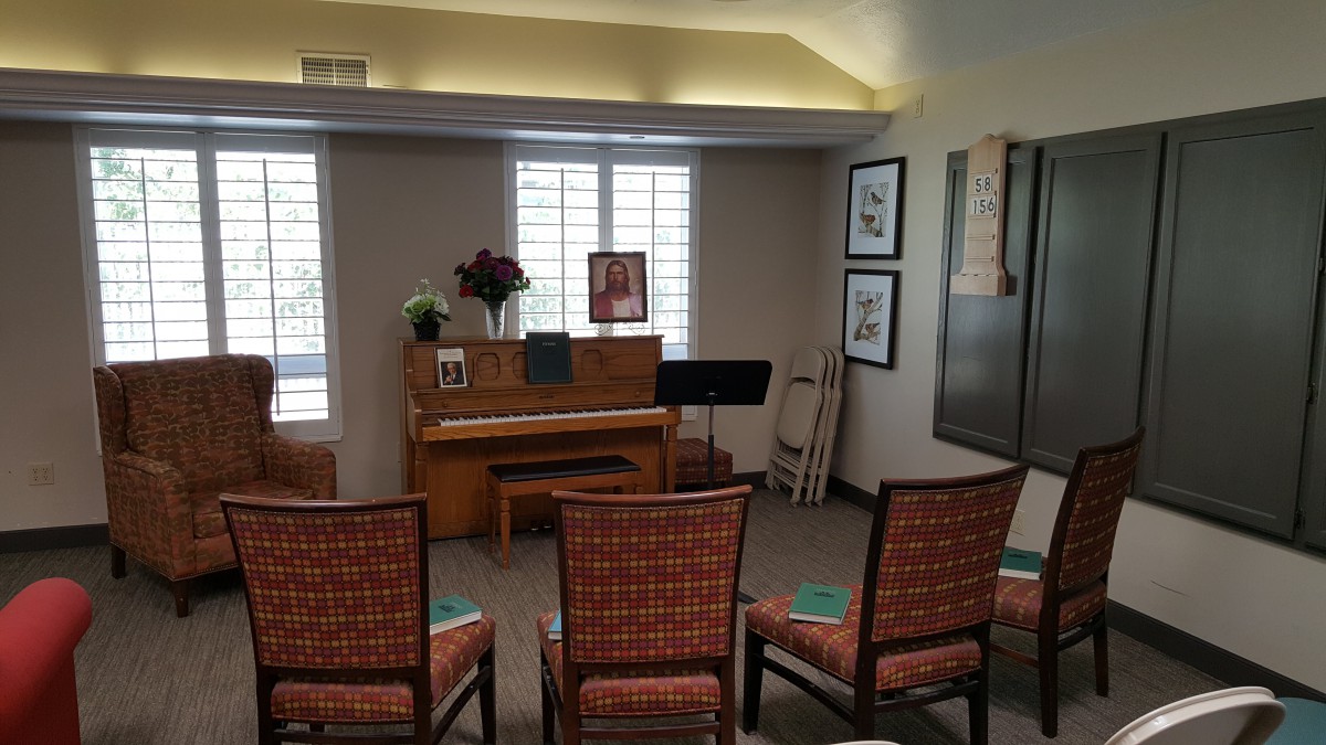 A cozy room with a piano, chairs arranged for an audience, and a music stand.