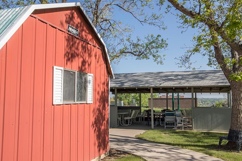 A sunny outdoor scene featuring a red building with a nearby shaded patio area.