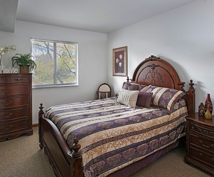 A cozy bedroom with a wooden bed, dresser, and a window allowing natural light.