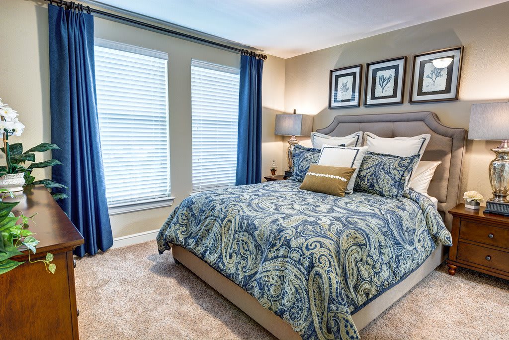A cozy bedroom featuring a bed with patterned bedding, blue curtains, and elegant wall art.