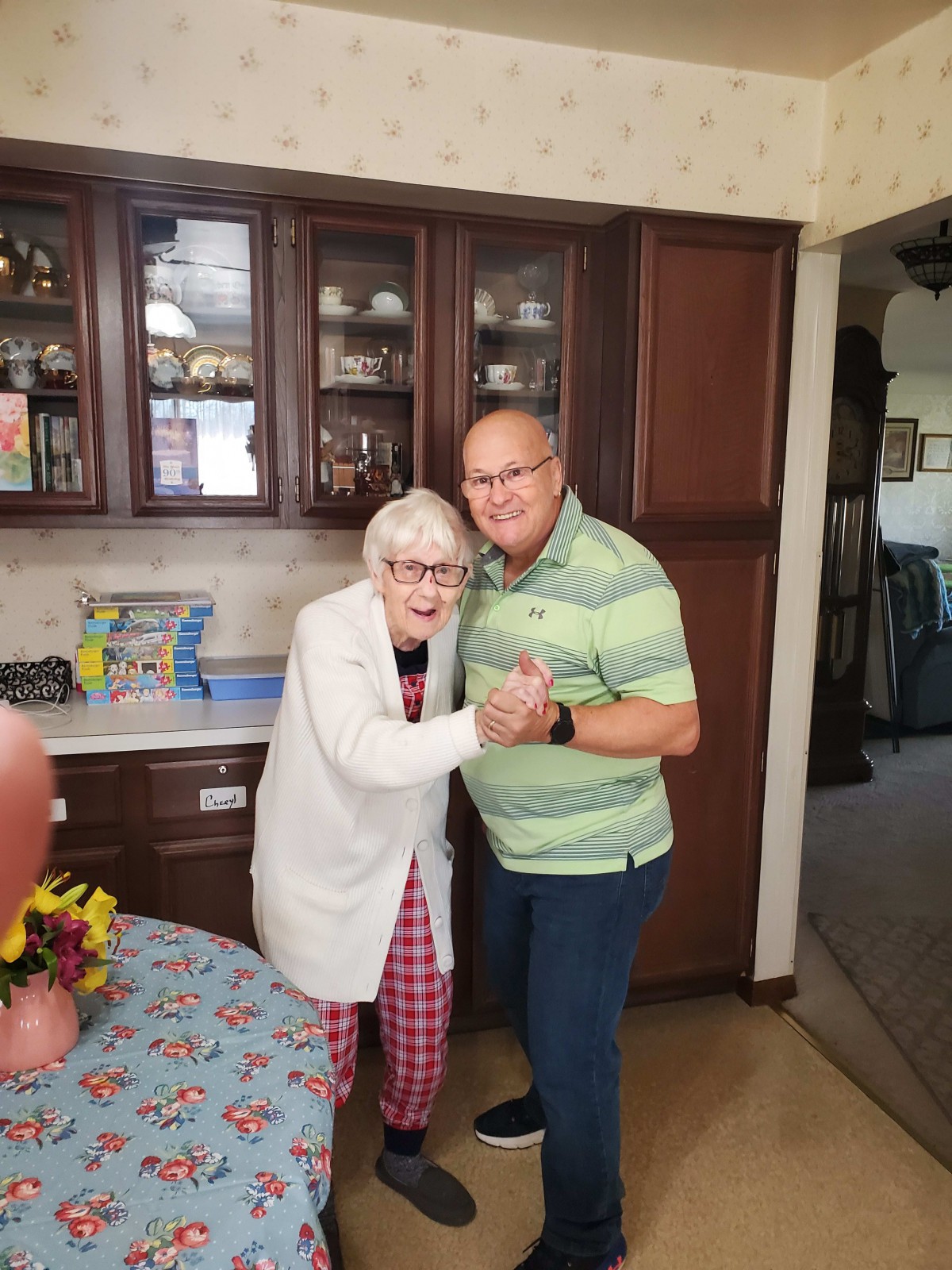 An elderly woman and a man posing together in a kitchen, both smiling.
