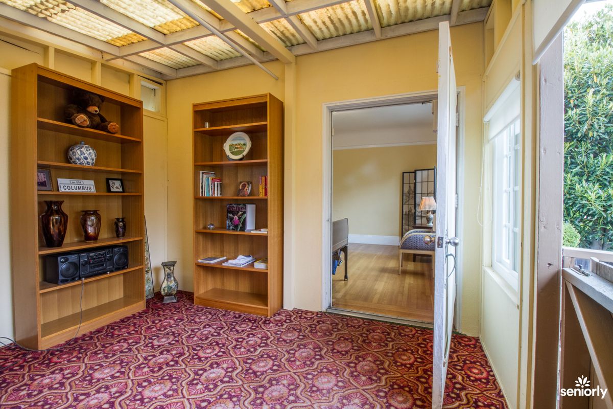 A cozy room with an open door, featuring bookshelves and a red patterned carpet.