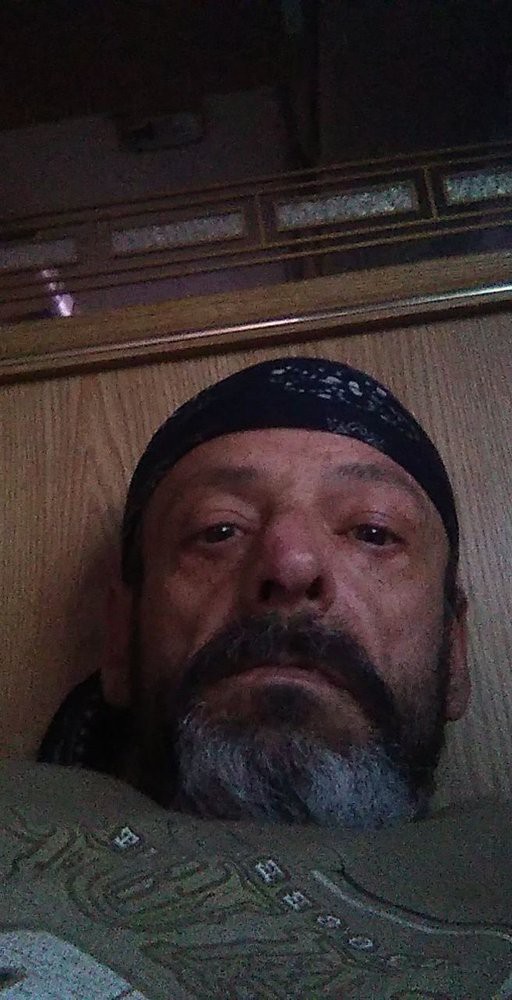 A man with a beard and bandana takes a selfie indoors.