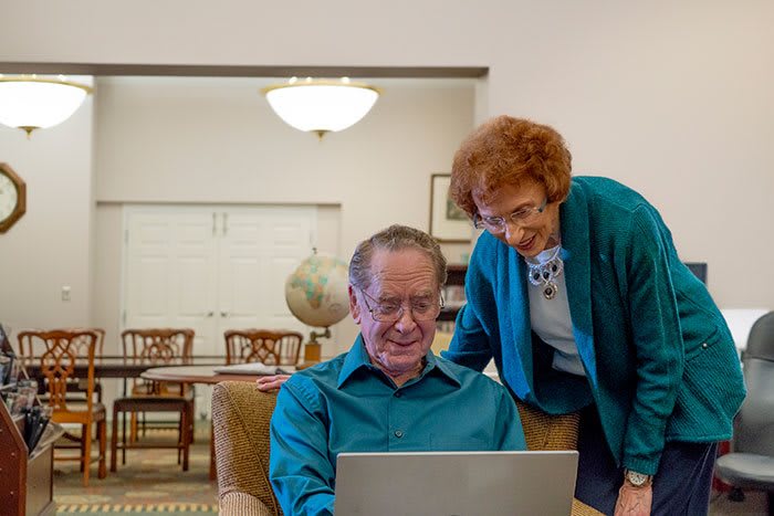 An elderly couple enjoying time together while using a laptop in their living room.