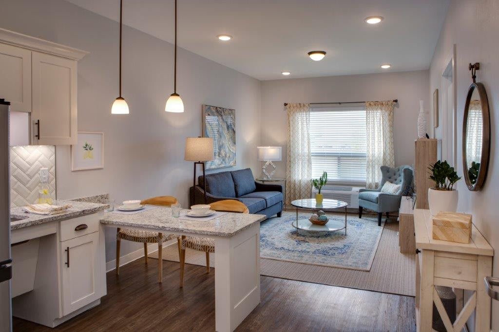 A cozy and modern living room featuring an open floor plan with a kitchen island, pendant lighting, and comfortable seating.