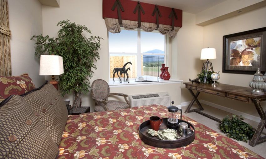 A cozy living room with decorative elements, including a patterned tablecloth, indoor plants, and horse figurines by the window.