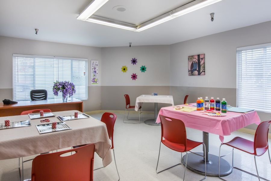 A classroom setting with tables and chairs, decorated with colorful art supplies and wall decorations.