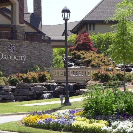A beautifully landscaped garden with vibrant flowers, a small bridge, and a lamp post in front of a building.
