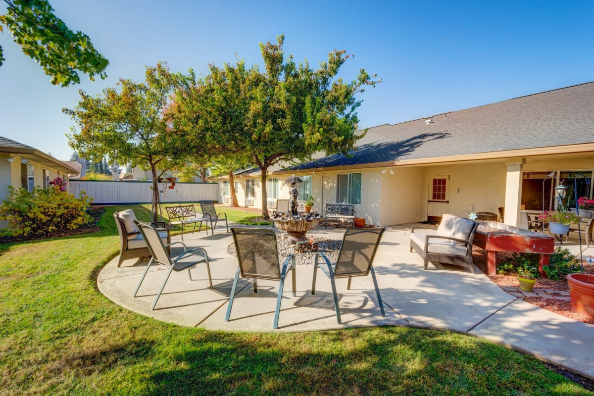 A sunny backyard patio with outdoor seating and trees.