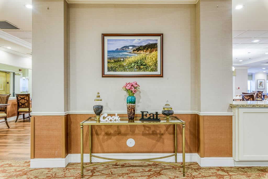 A stylish interior setup featuring a decorative table, a vase of flowers, and a framed landscape picture on the wall.